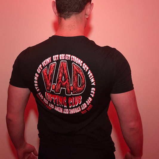A man viewed from behind wearing a black t-shirt with a large red and white graphic on the back that reads 'V.A.D lifting club'